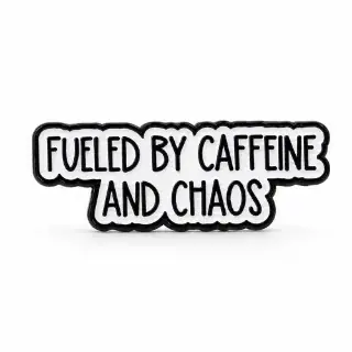 White Fuelled by Caffeine and Chaos enamel pin with black lettering and outline on a plain white background.